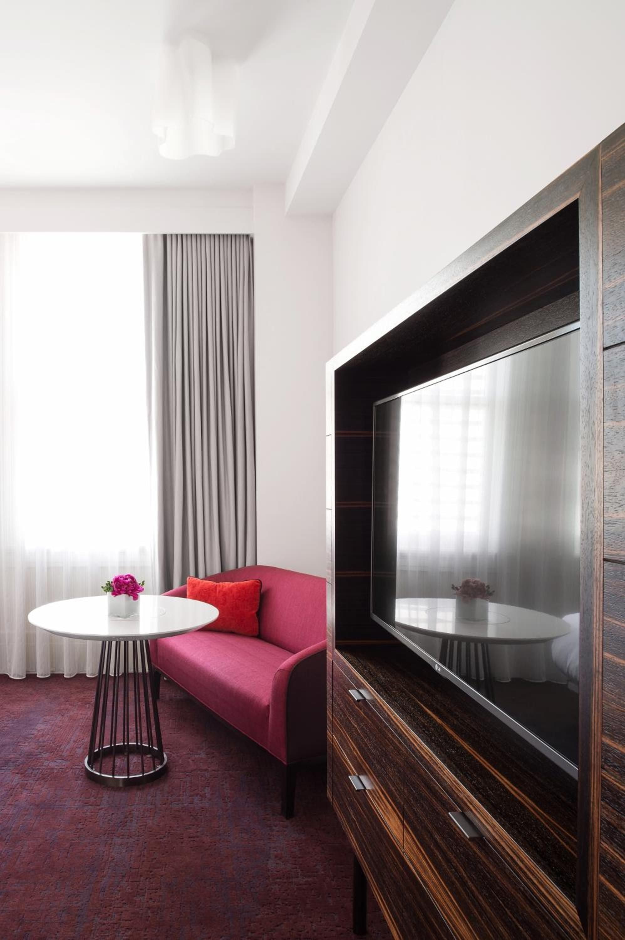 Vibrant fuchsia seating pops against rich walnut millwork in this contemporary guest room, where clean lines meet bold color choices and natural light softens modern edges.