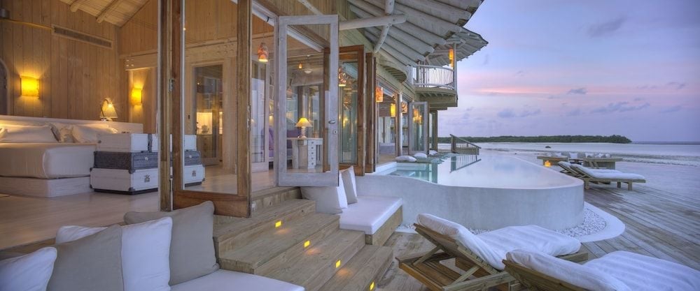Infinity pools mirror twilight skies from overwater villa decks, where warm wood meets crystalline waters and barefoot luxury unfolds beneath the Maldivian evening.