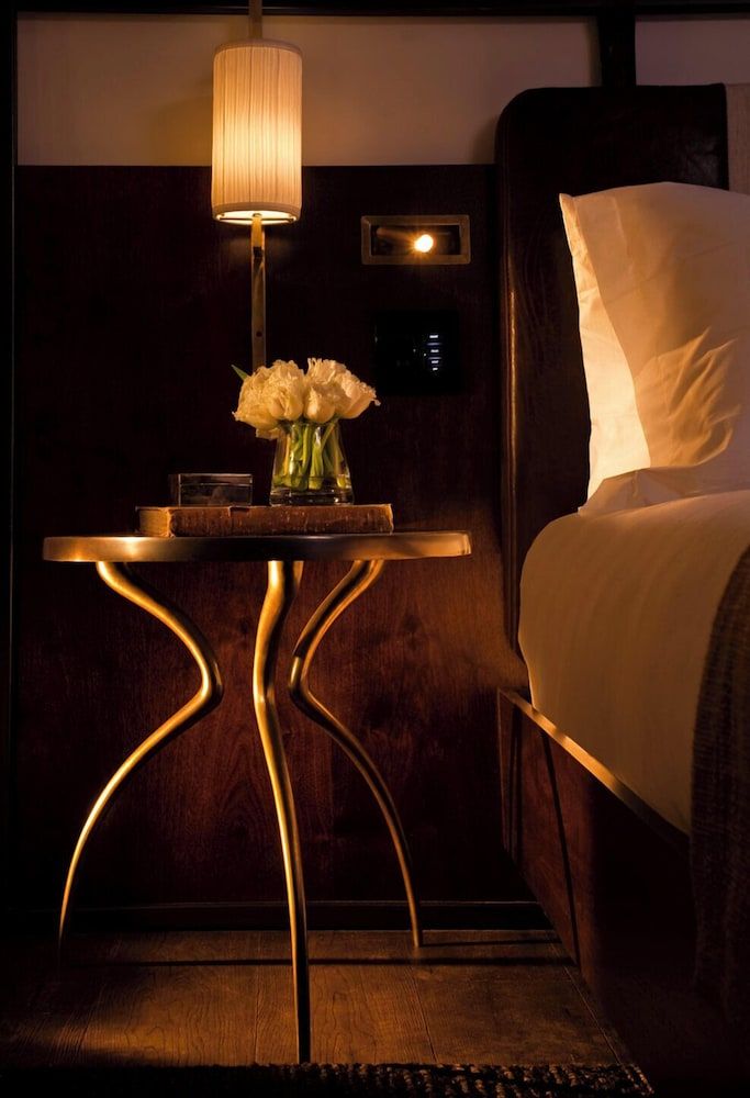 Warm lamplight illuminates a sculptural side table crowned with fresh peonies, where curved brass legs meet rich wood grain in perfect harmony.