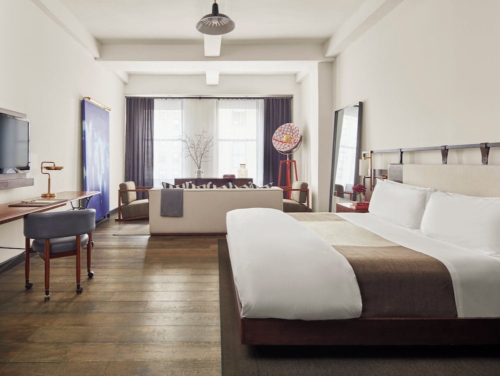 Exposed beams and rich hardwood floors create industrial-chic elegance in this spacious suite, where vintage-inspired furnishings meet modern luxury beneath soaring ceilings.