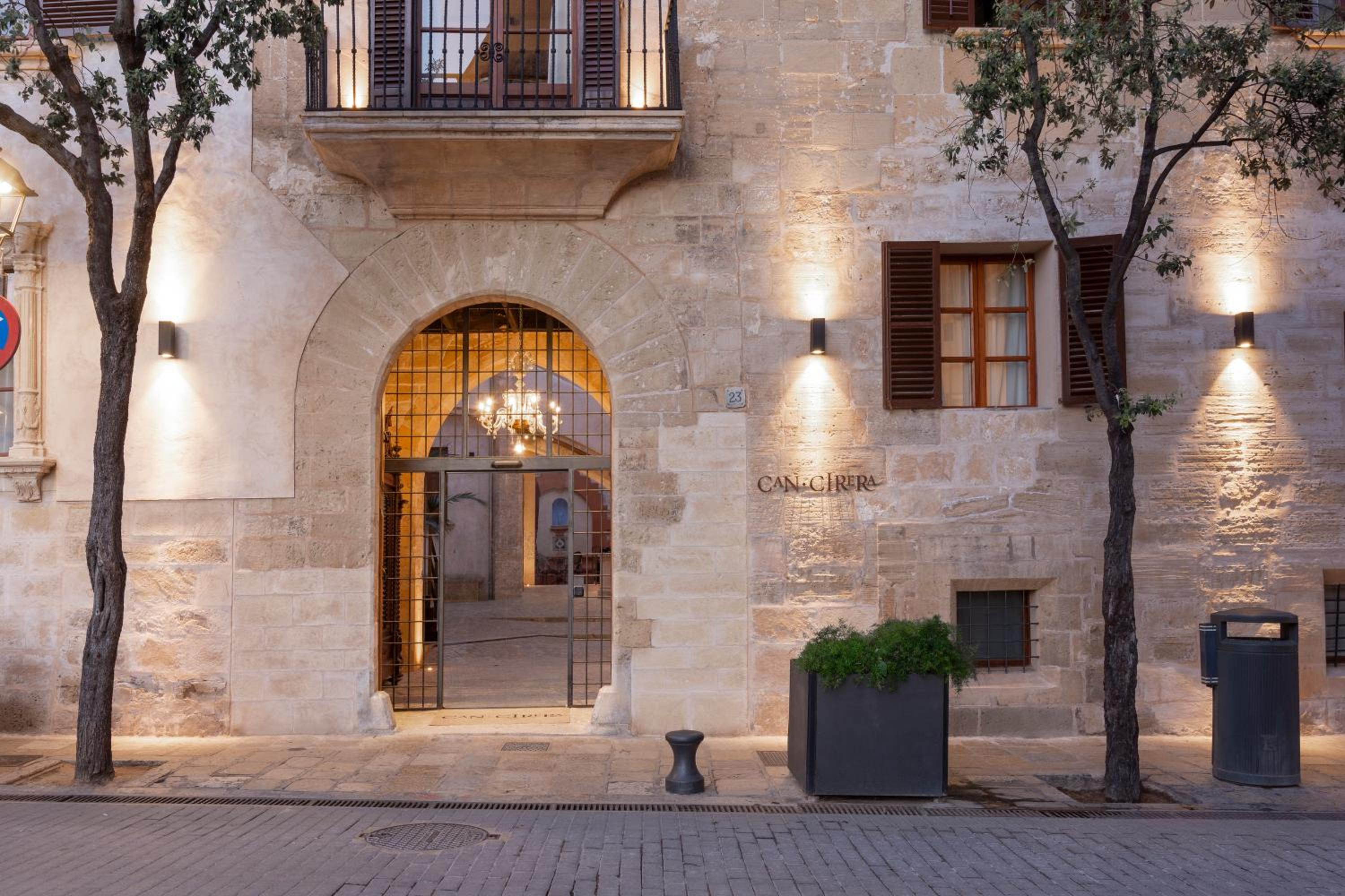 Warm limestone glows under evening lights as Hotel Can Cera's graceful arched entrance welcomes guests into this beautifully restored Mallorcan palace.