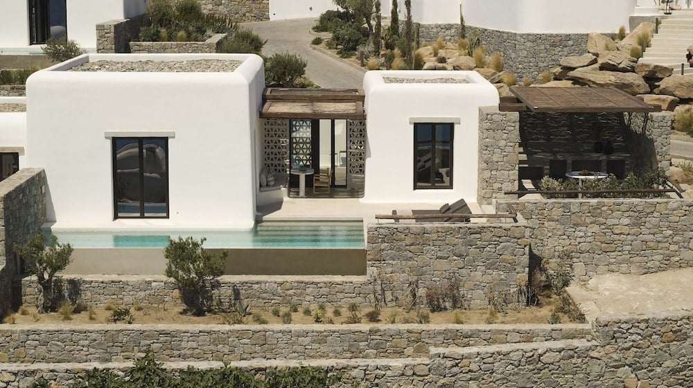 Whitewashed cubic suites cascade down ancient stone terraces, each with private infinity pools that seem to float above Mykonos' windswept landscape.