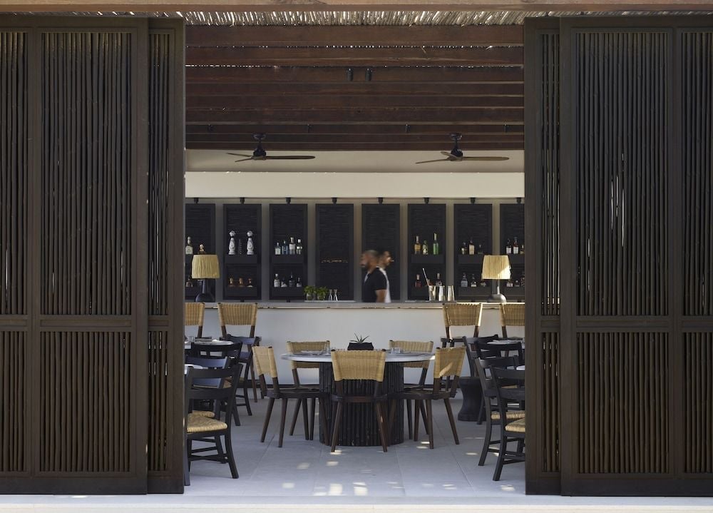 Natural wood screens frame the resort's sophisticated restaurant, where woven chairs and ambient lighting create an intimate dining sanctuary beneath exposed timber beams.