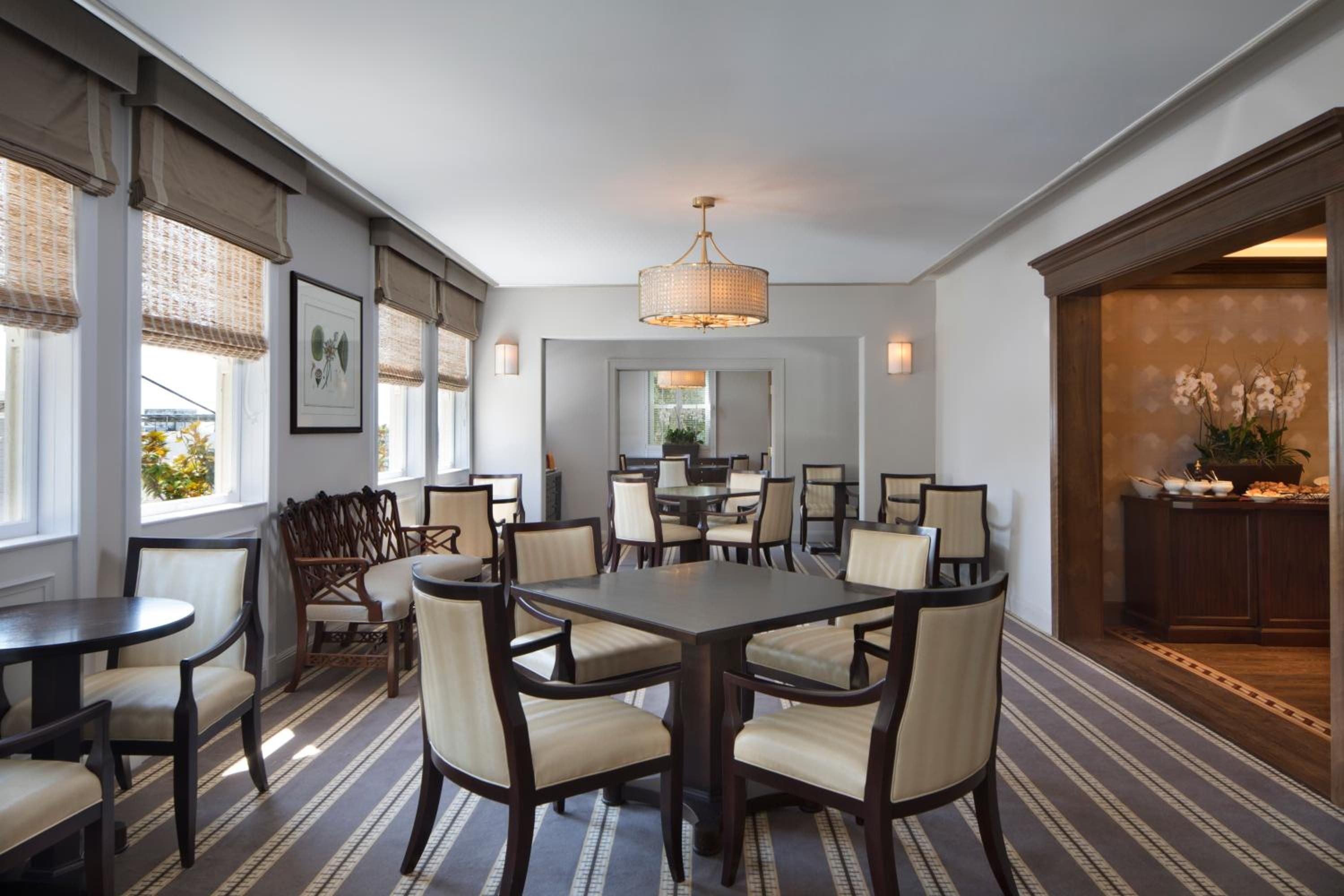 Natural light streams through woven bamboo shades onto crisp white linens and dark wood furnishings, creating an intimate dining atmosphere that feels both sophisticated and welcoming.
