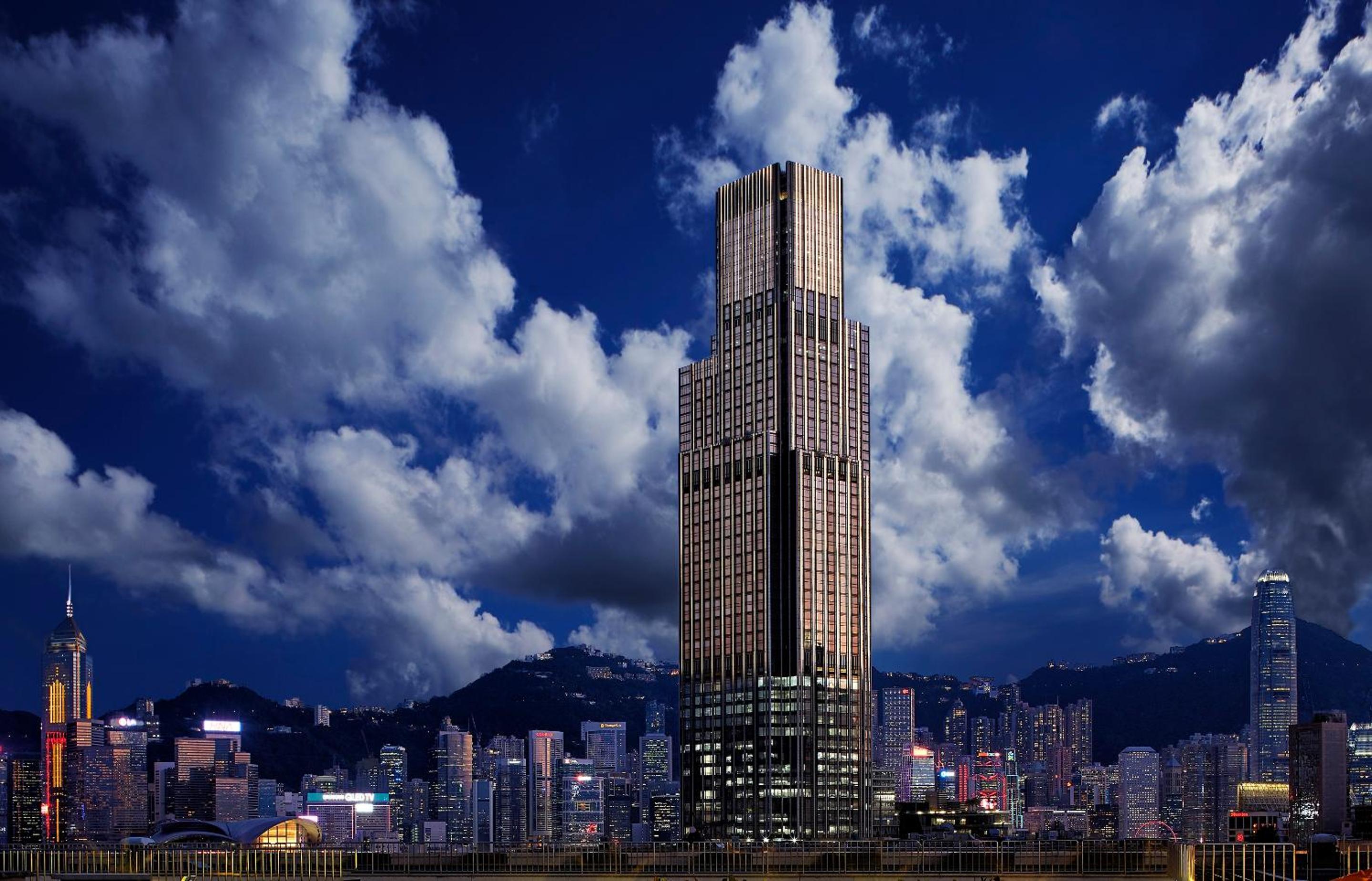 Soaring above Victoria Harbour's glittering skyline, this architectural marvel commands the horizon with its distinctive copper-toned facade against dramatic evening clouds.