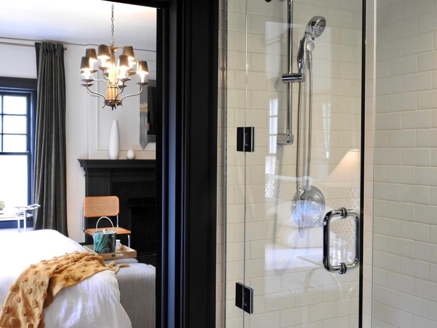Glass-enclosed showers open directly onto the bedroom, while subway tiles and chrome fixtures create an intimate yet luxurious bathing experience.