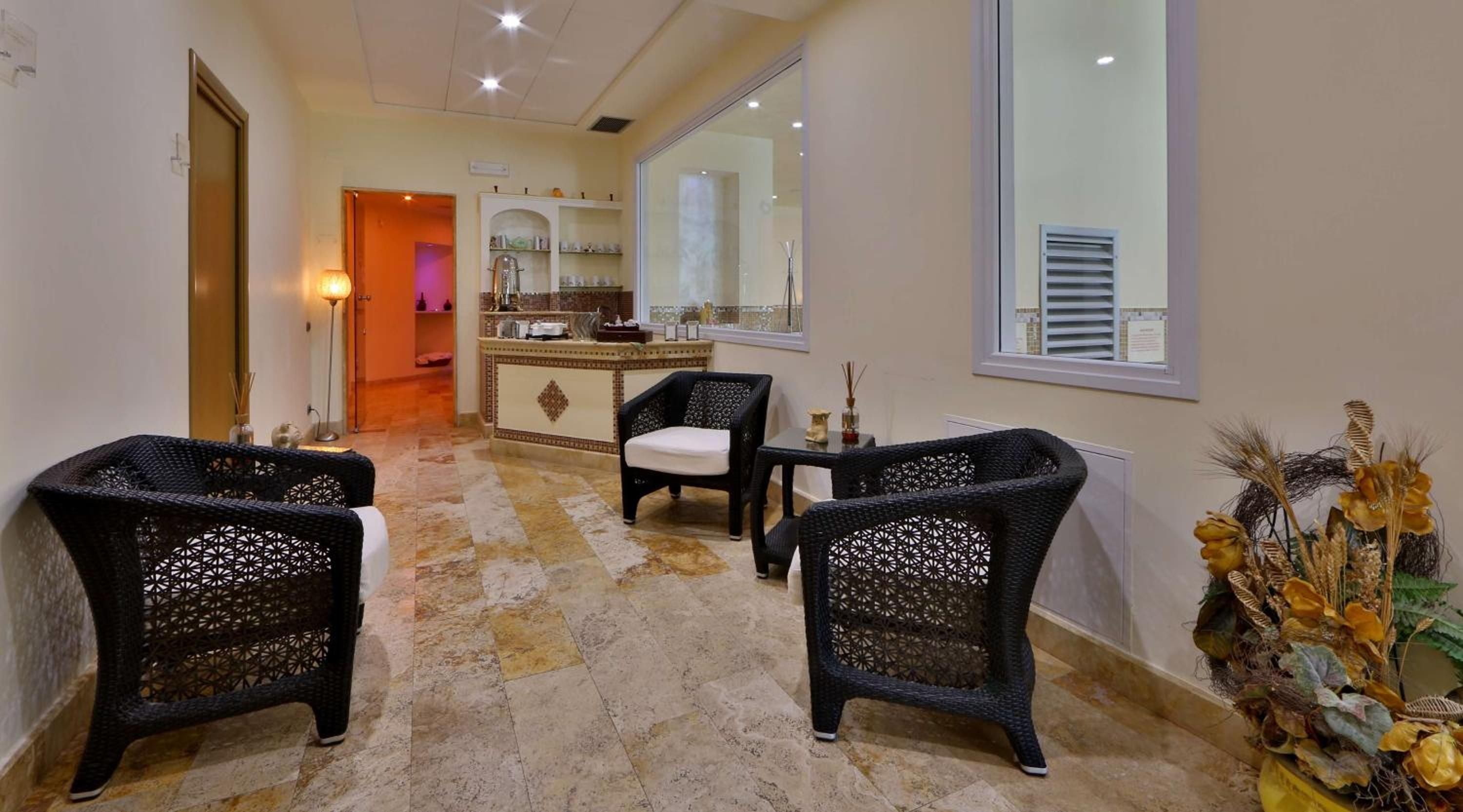 Wicker loungers with intricate geometric patterns create intimate conversation nooks in the spa's serene waiting area, where natural stone floors and soft lighting set a tranquil mood.