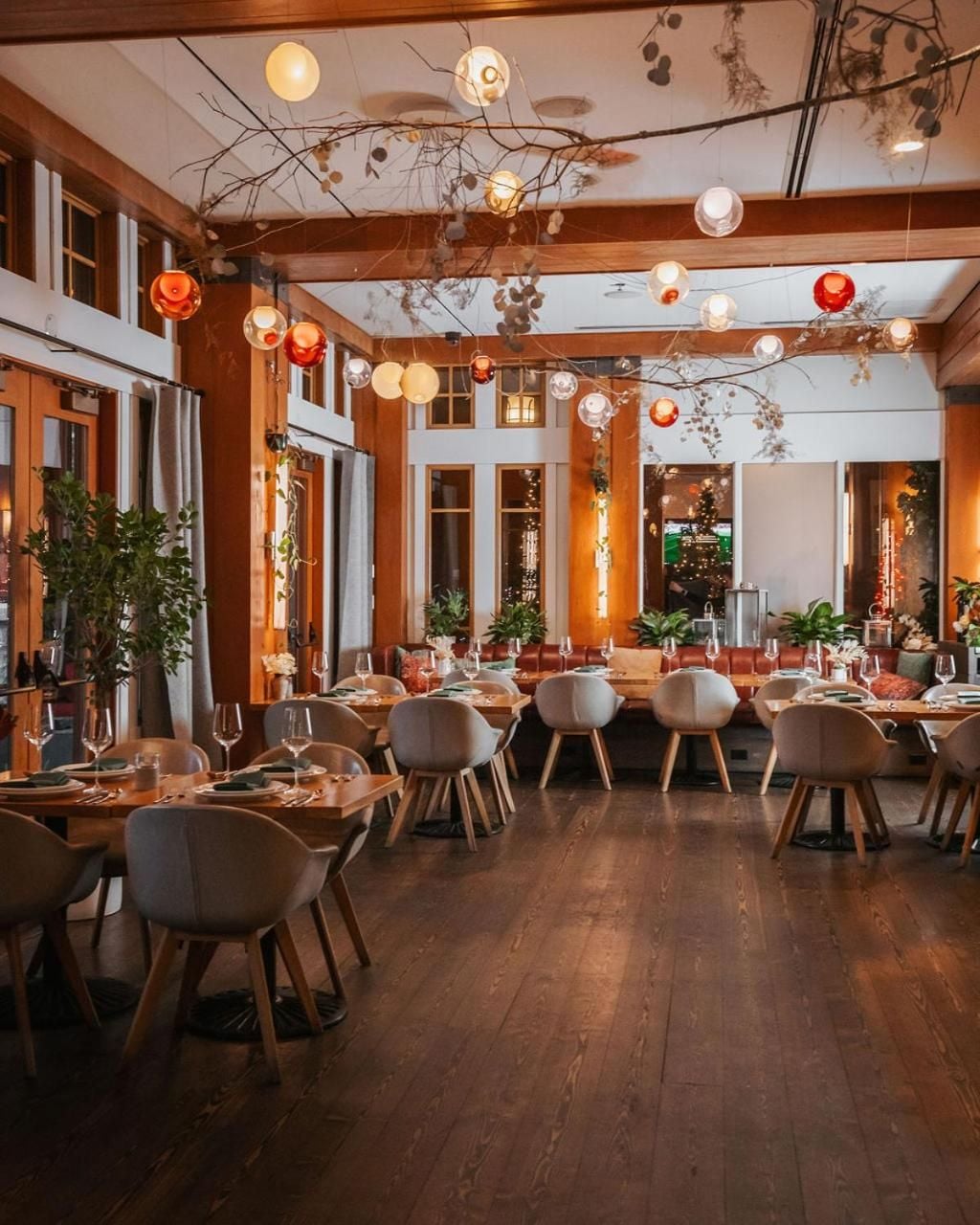 Warm pendant lights dance above rustic wooden tables while exposed beams and natural branches create an intimate dining atmosphere that feels both refined and welcoming.