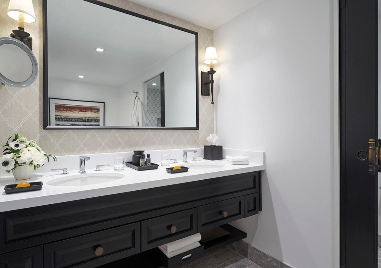Crisp white quartz countertops and charcoal cabinetry create a sophisticated contrast in guest bathroom vanities, while geometric wallpaper adds subtle texture beneath warm sconce lighting.