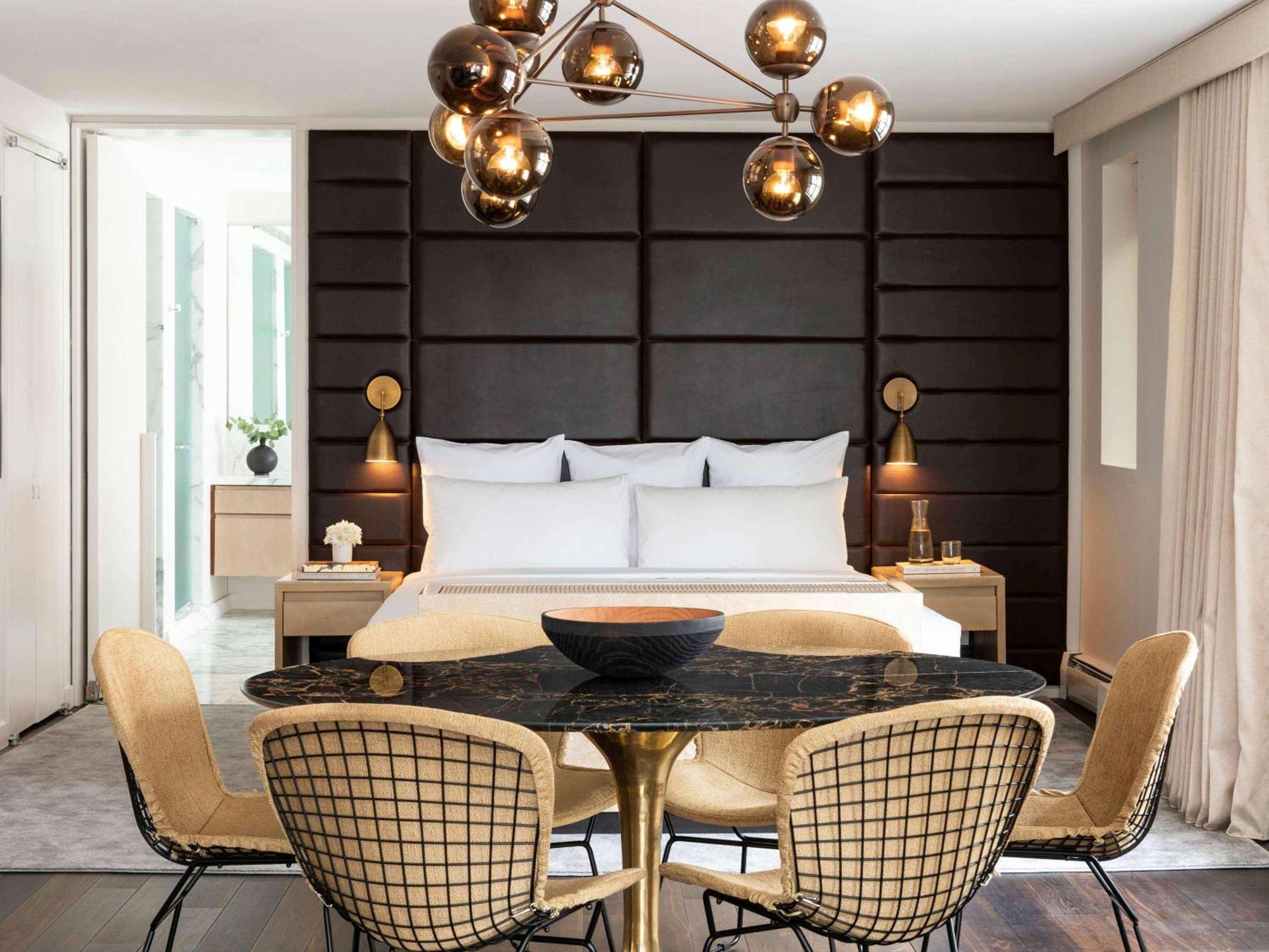 Warm amber globe lights cast an intimate glow over the suite's dramatic charcoal headboard wall, while brass fixtures and marble surfaces create sophisticated contrast.