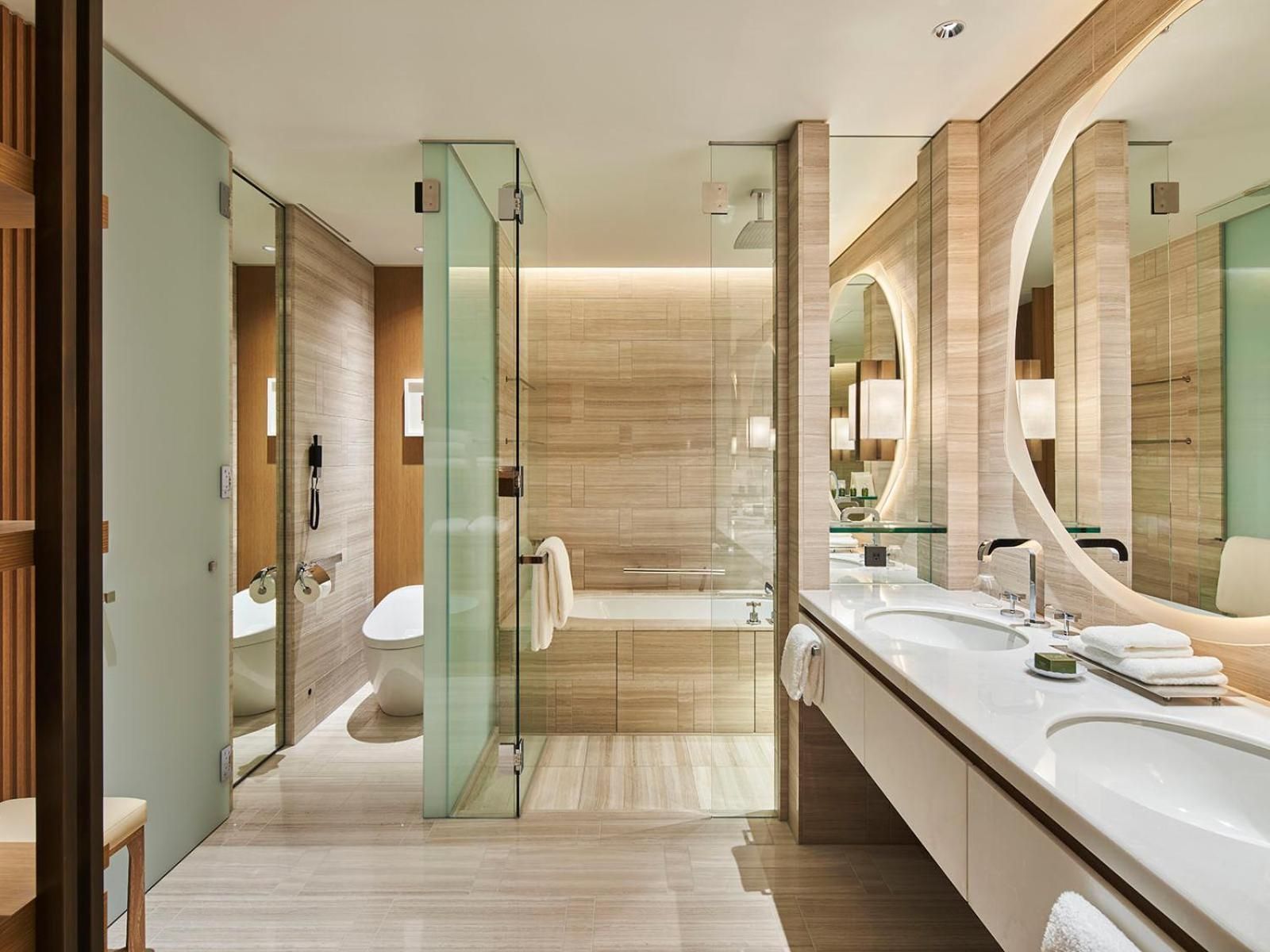 Warm wood tones and frosted glass create serene harmony in this spa-like retreat, where rainfall showers and floating vanities embody Japanese minimalist luxury.