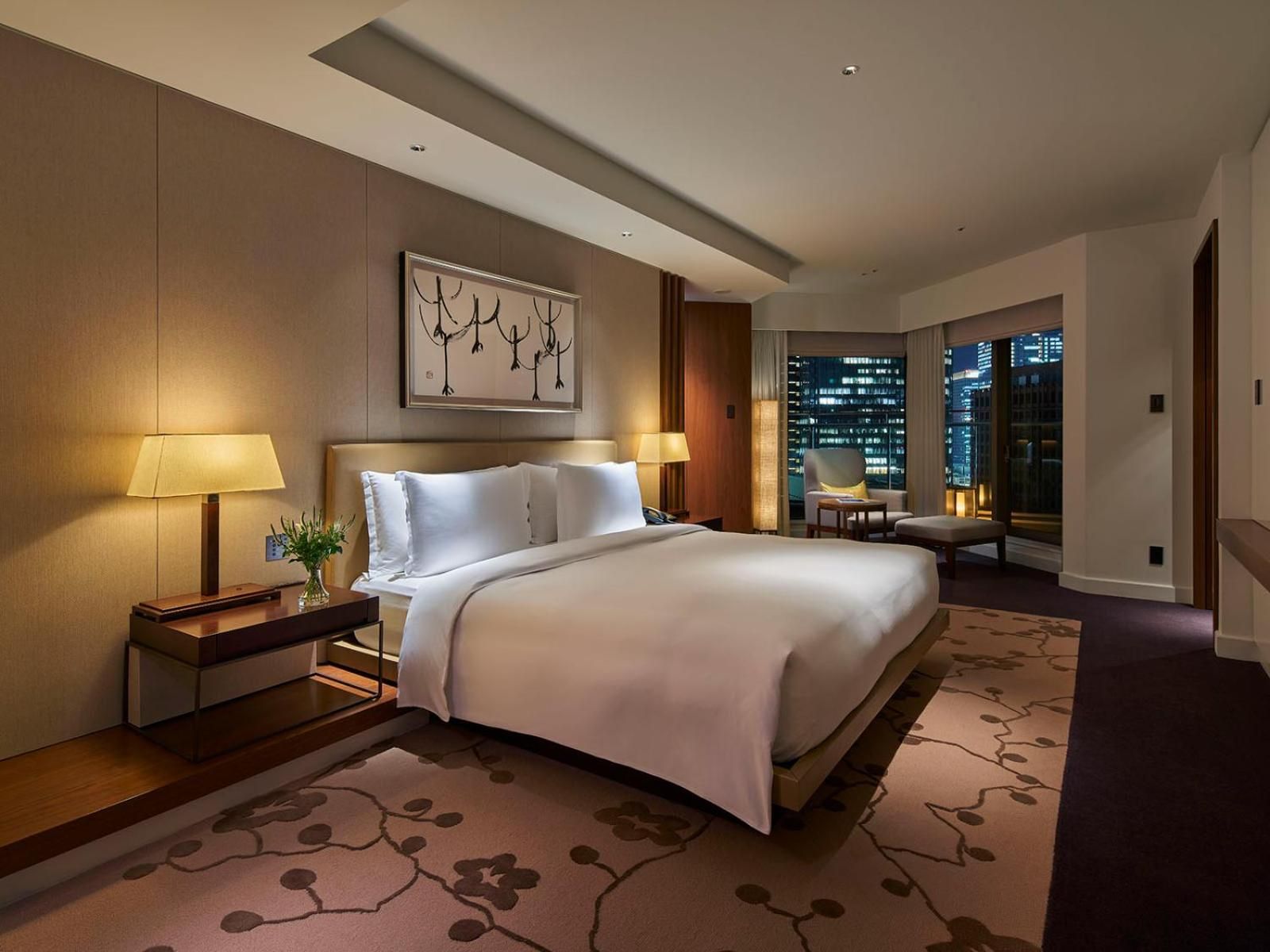 Warm ambient lighting and floor-to-ceiling windows frame Tokyo's glittering skyline from this elegantly appointed suite, where cherry blossom motifs dance across plush carpeting.