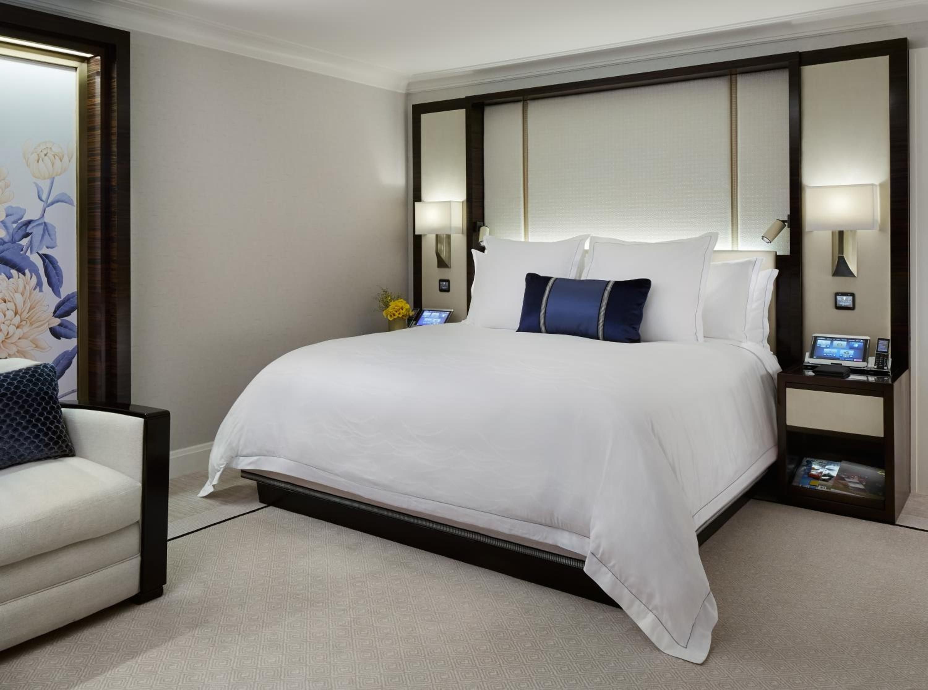 Crisp white linens and navy accents create serene sophistication, while integrated nightstand technology and floral artwork add modern luxury to this tranquil retreat.