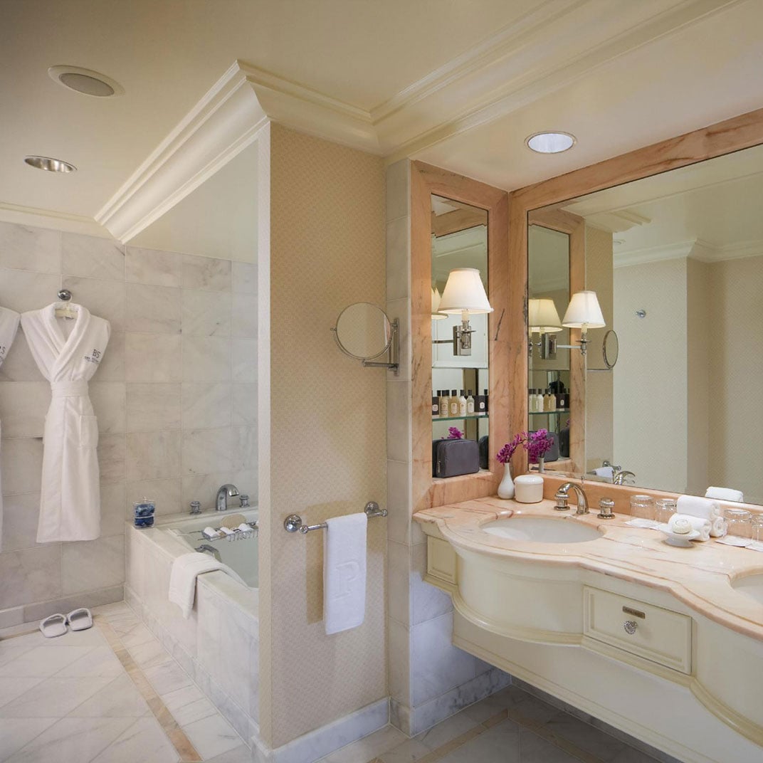 Marble surfaces gleam under soft recessed lighting while a plush bathrobe awaits beside the soaking tub, epitomizing Beverly Hills luxury in intimate detail.