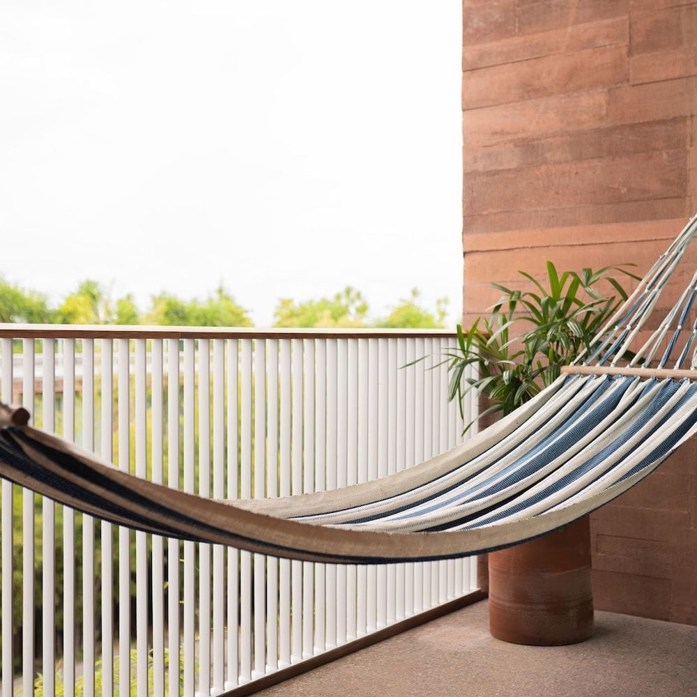 Striped hammock sways gently on a private terrace, where warm brick walls and tropical greenery frame lazy afternoon moments overlooking Bali's verdant landscape.