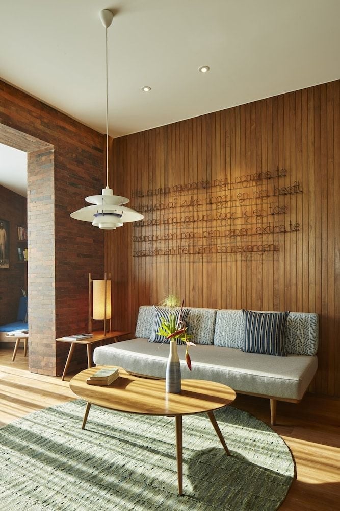 Warm teak paneling and mid-century furnishings create an intimate lounge where Scandinavian design meets tropical sophistication, bathed in golden afternoon light.