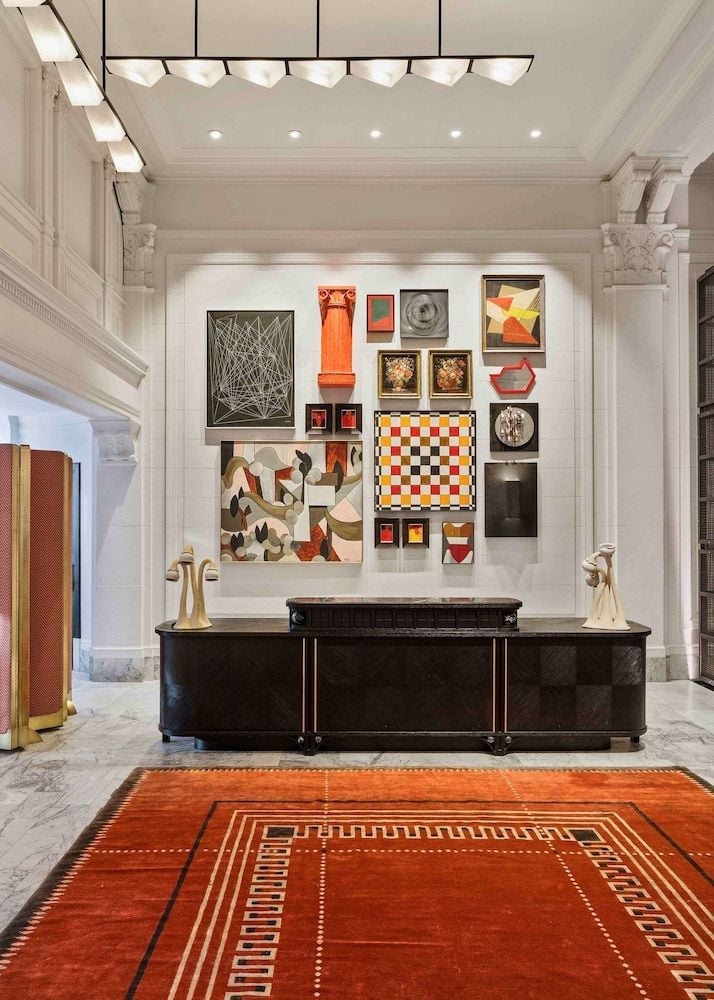 Curated contemporary artworks create a gallery-like atmosphere in the marble-clad lobby, where bold geometric patterns on the handwoven rug echo the eclectic wall collection above.