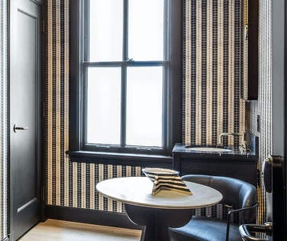 Striped wallpaper in charcoal and cream creates intimate drama in this corner nook, where a marble-topped table catches afternoon light streaming through vintage-style windows.