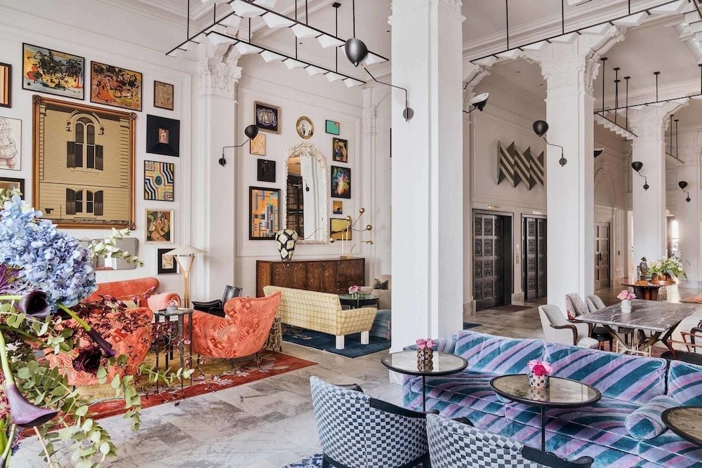 Eclectic art collections and jewel-toned furnishings create an inviting salon atmosphere beneath soaring arched ceilings and contemporary pendant lighting fixtures.