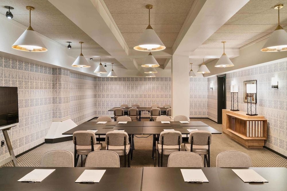 Geometric wallpaper and warm brass pendant lights create an intimate boardroom atmosphere where exposed beams meet contemporary sophistication in this thoughtfully designed conference space.