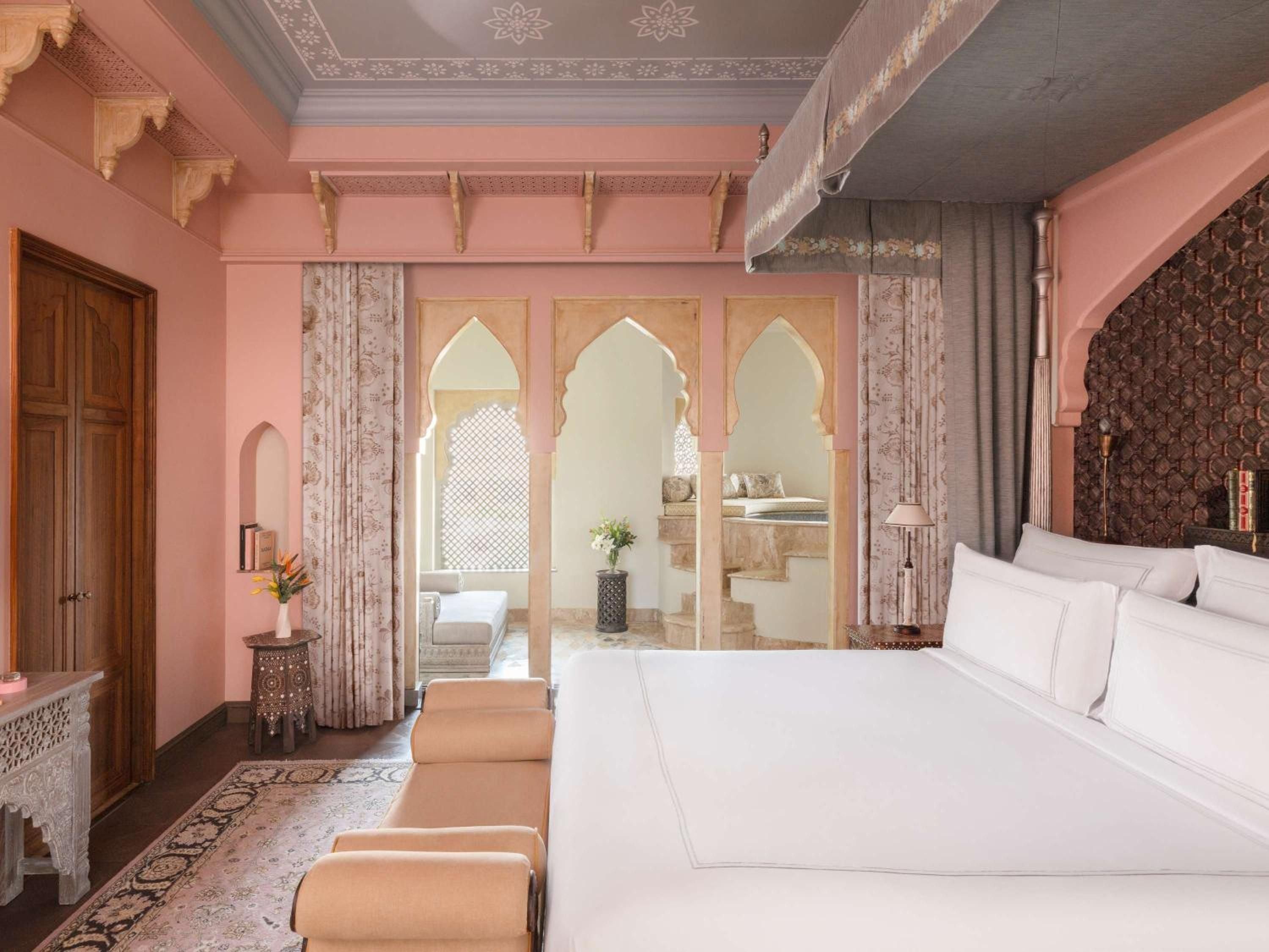 Moorish arches frame a marble bathroom sanctuary where rose-hued walls meet intricate carved details, creating an intimate palace retreat with crisp white linens.