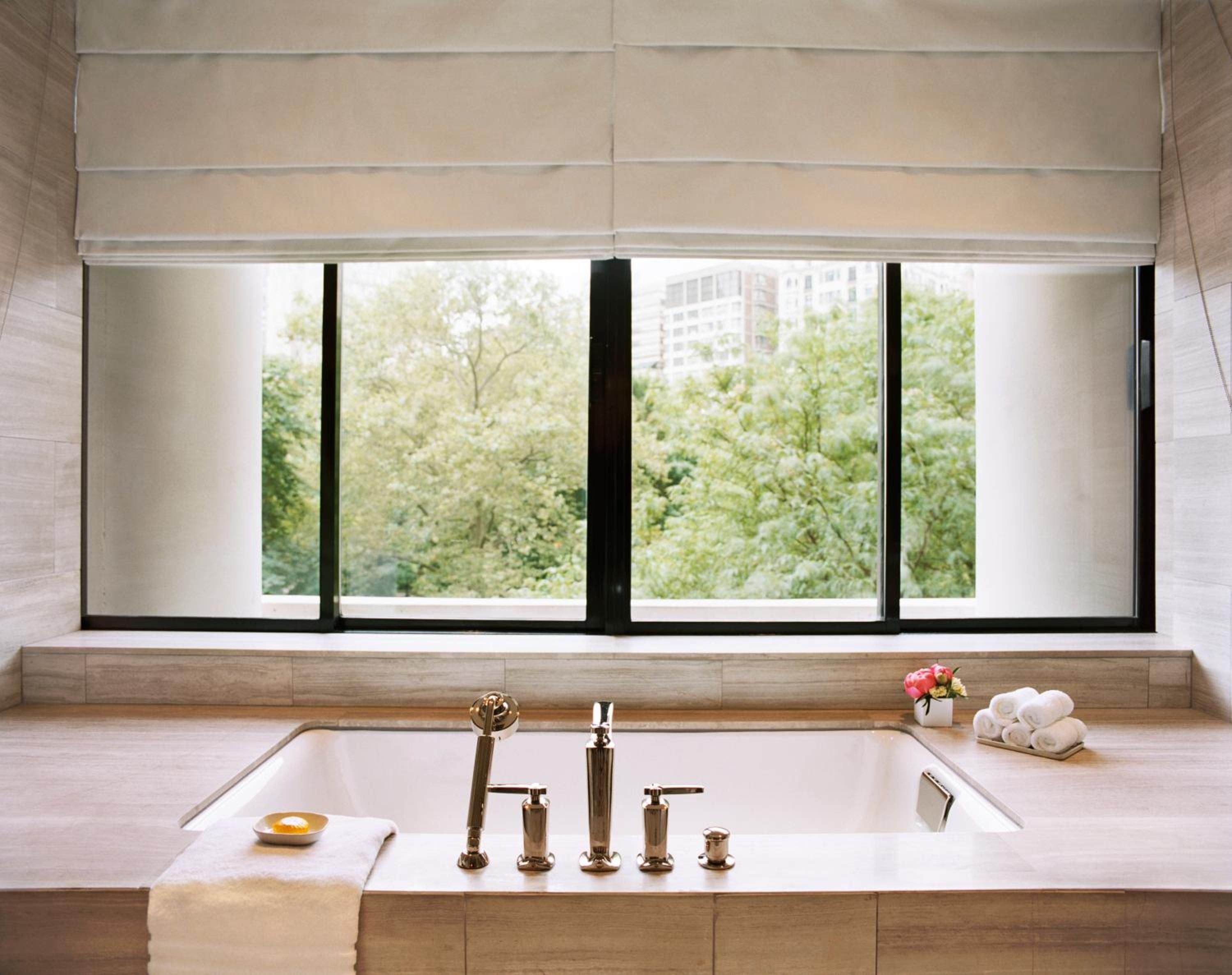 Marble surrounds and brass fixtures frame a soaking tub overlooking Rittenhouse Square's canopy, where urban luxury meets park tranquility through floor-to-ceiling windows.
