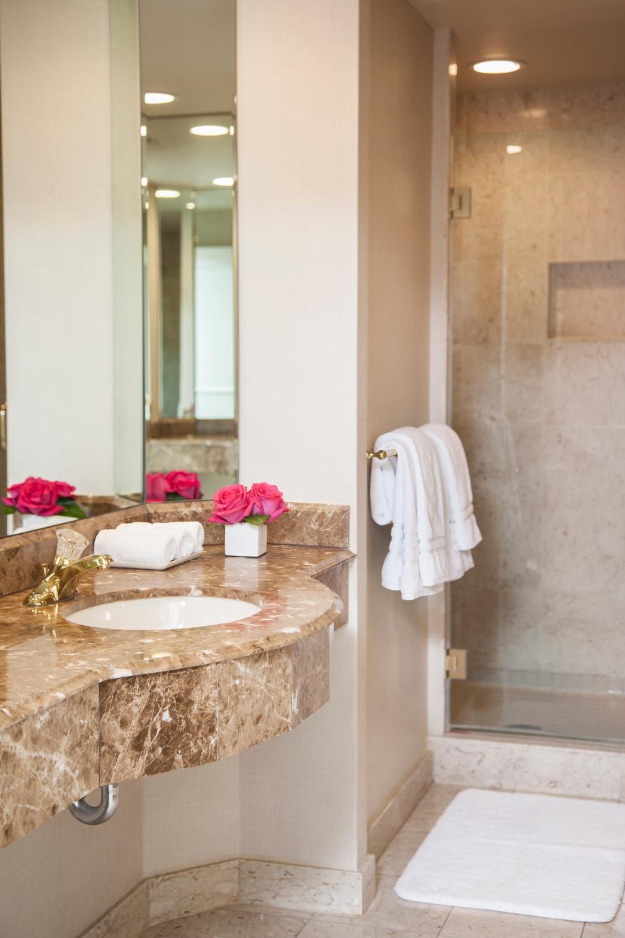 Warm marble surfaces and brass fixtures create an intimate powder room where fresh pink roses add a touch of romance to the sophisticated stone vanity.