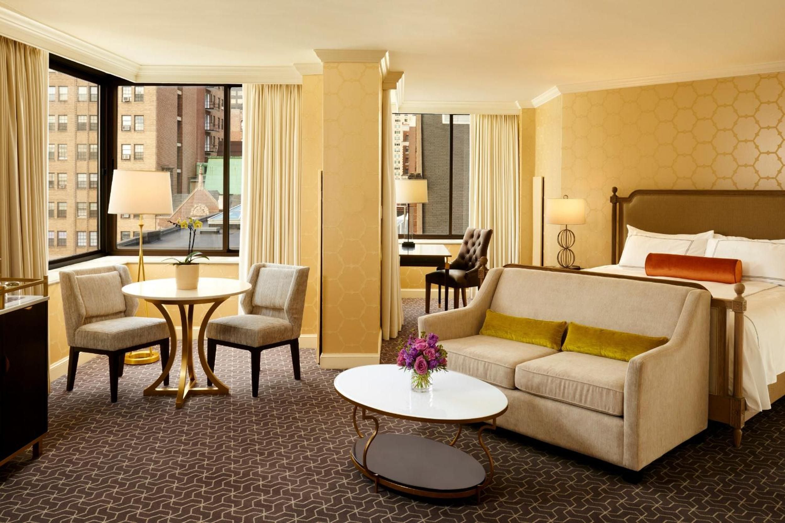 Golden afternoon light floods this corner suite, where geometric carpeting meets honeyed wallpaper and city views stretch beyond floor-to-ceiling windows.