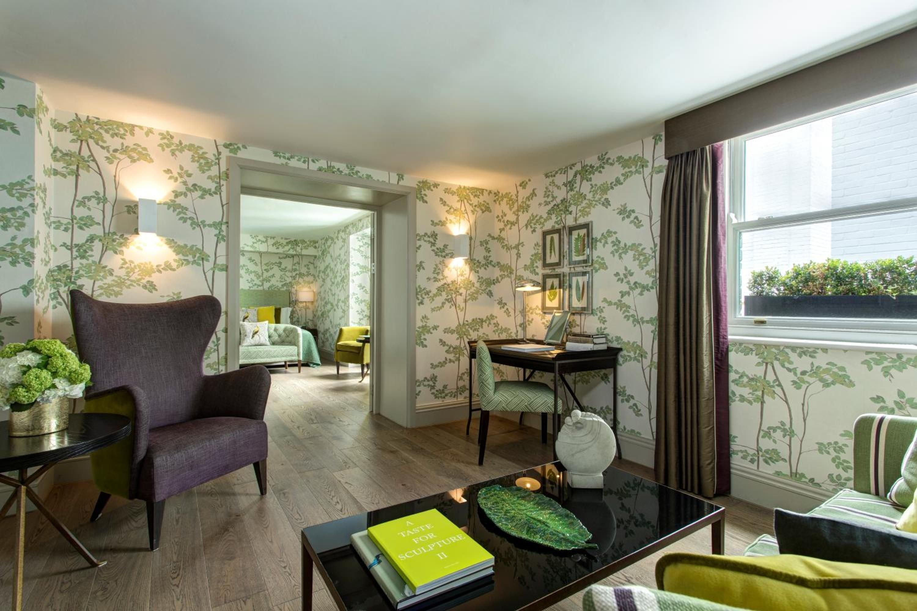 Botanical wallpaper creates an enchanted garden atmosphere in this elegantly appointed suite, where purple velvet armchairs and chartreuse accents add contemporary sophistication to classic English style.