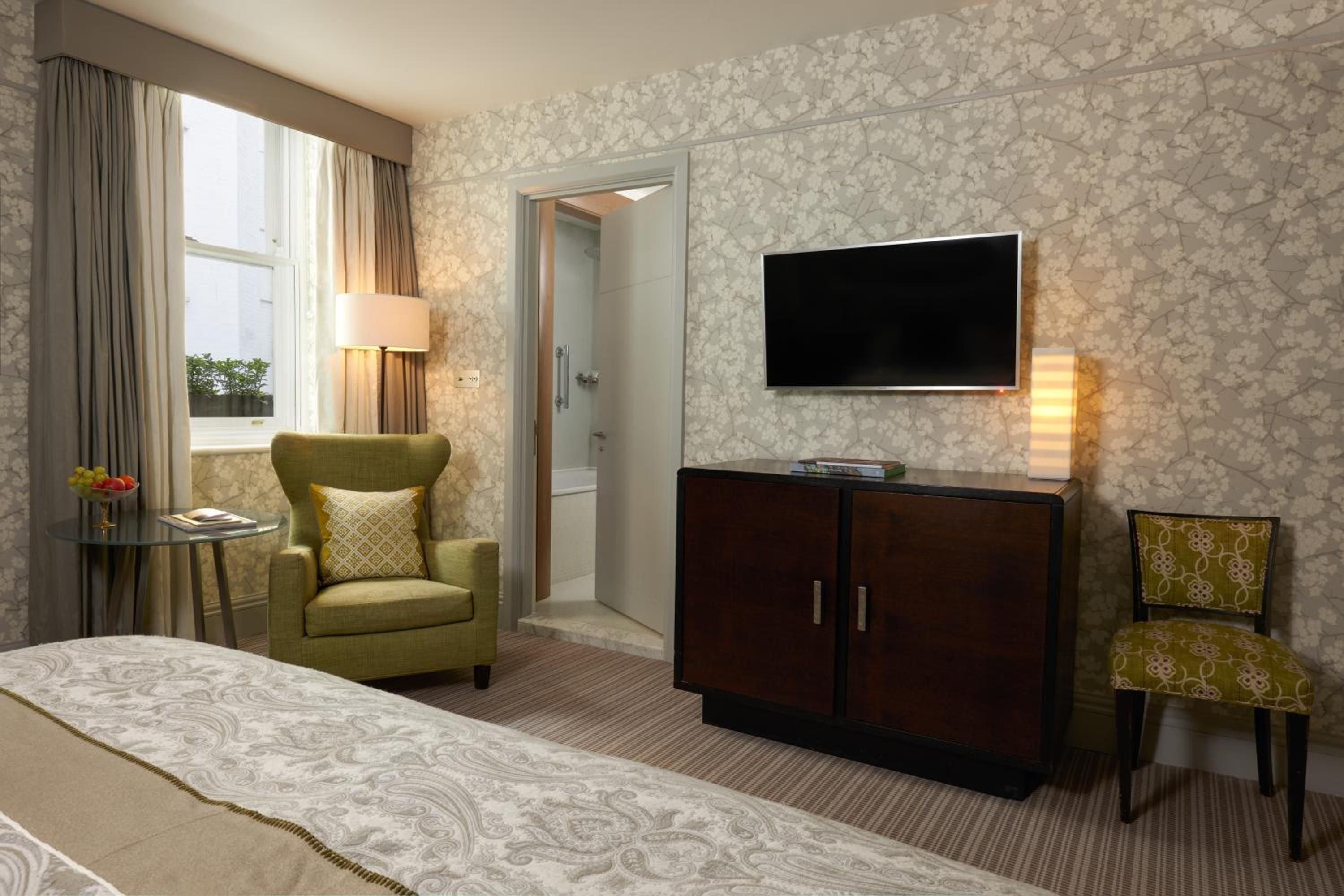 Olive-green armchairs and geometric wallpaper create sophisticated warmth in this elegantly appointed suite, where rich mahogany furnishings complement the hotel's timeless British heritage.