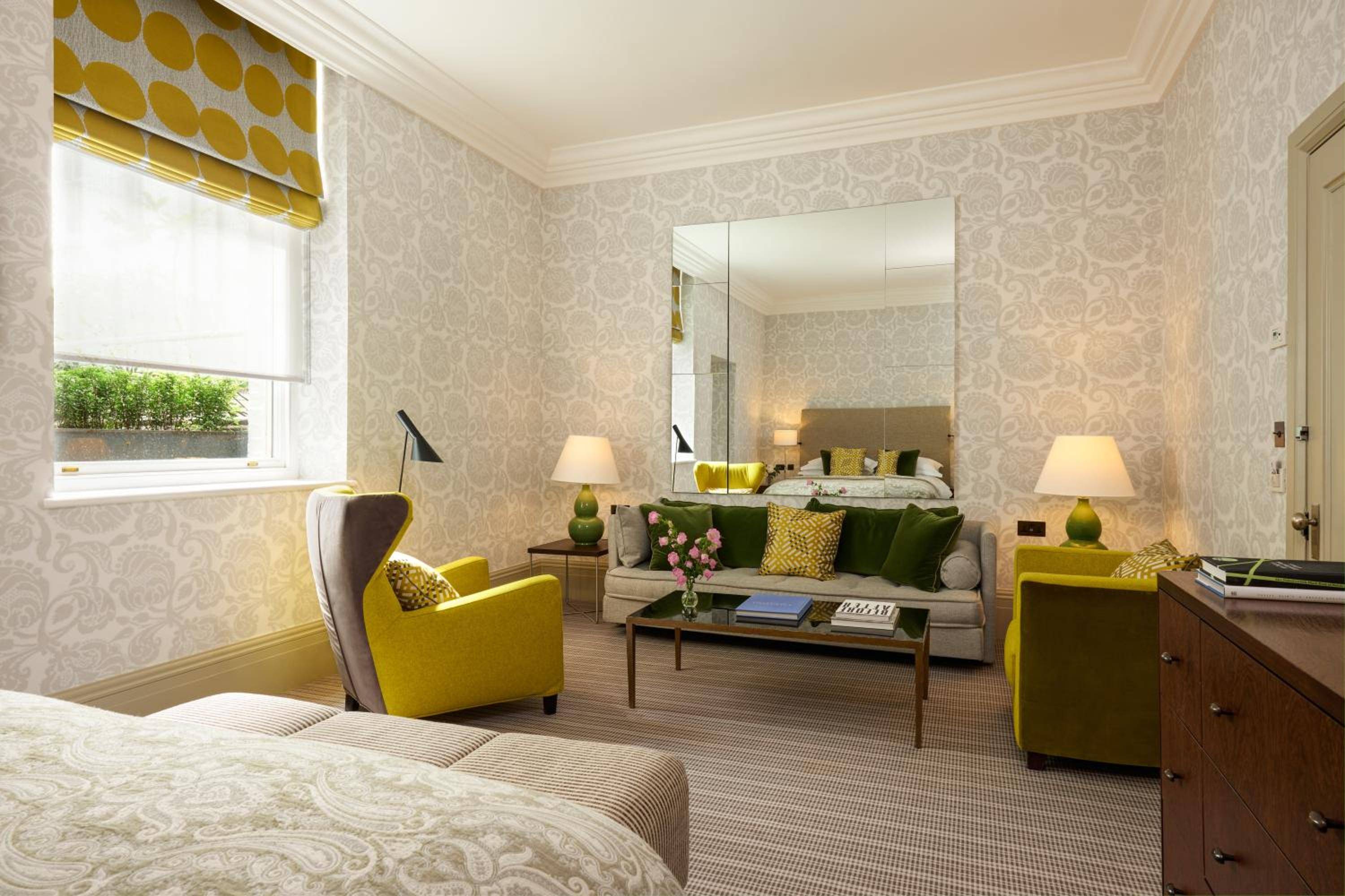 Sunlight streams through Georgian windows onto plush yellow armchairs and sage velvet sofas, where damask wallpaper creates an intimate cocoon of Mayfair elegance.
