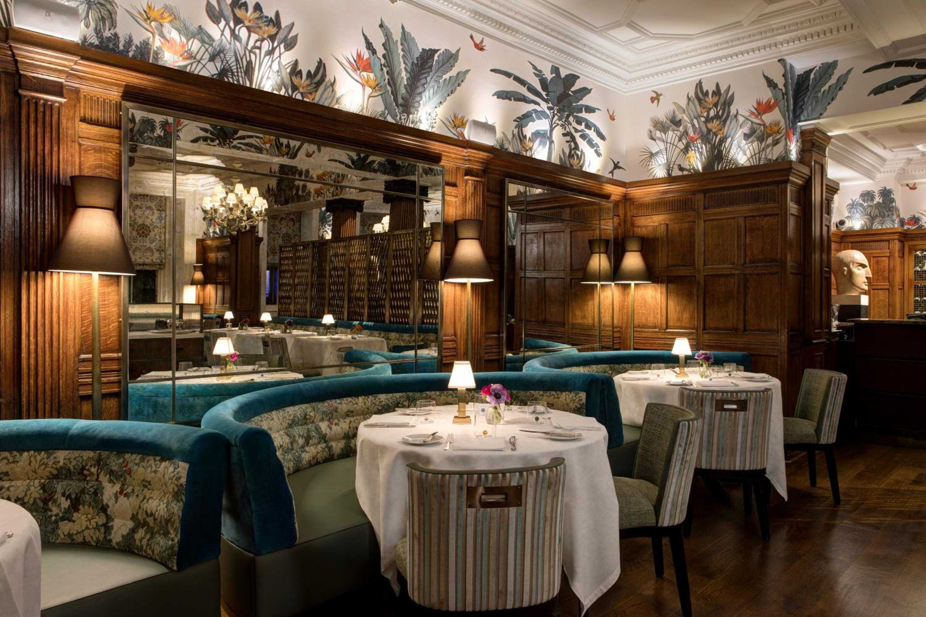 Rich walnut paneling meets tropical wallpaper at the refined dining room, where plush teal banquettes and intimate table lamps create an enchanting botanical sanctuary.