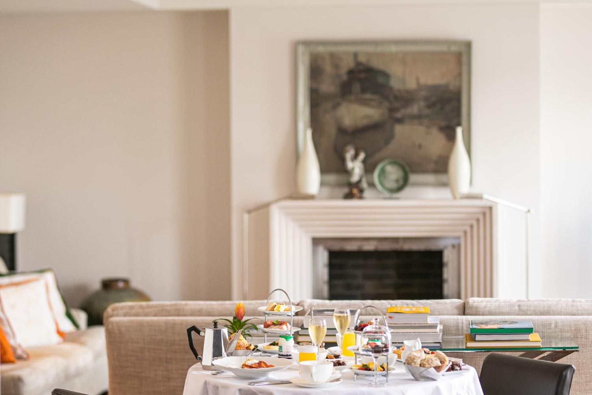 Afternoon tea service transforms this elegant sitting room, where champagne catches golden light against cream furnishings and classical artwork above the fireplace.