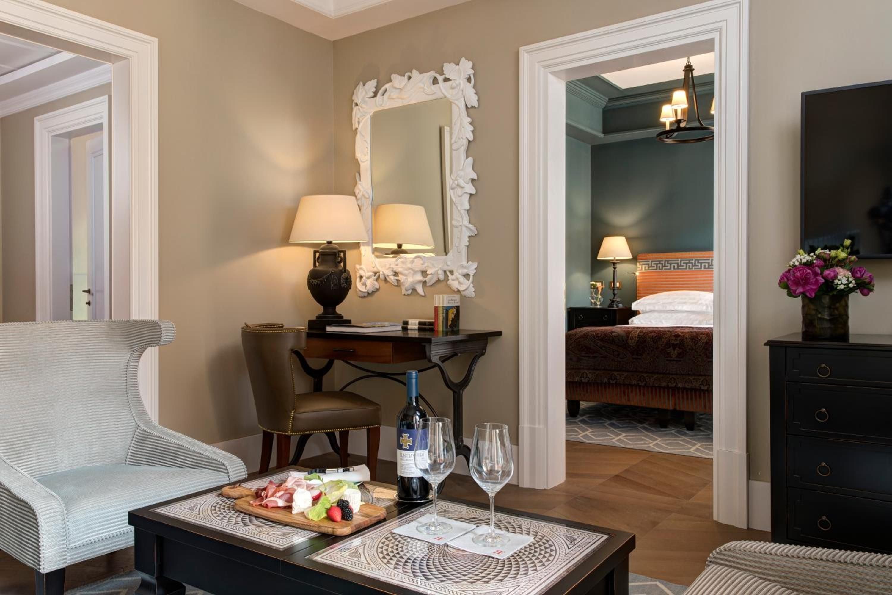 Ornate white mirrors and polished console tables create an elegant sitting area, where wine and charcuterie await in this thoughtfully appointed suite.
