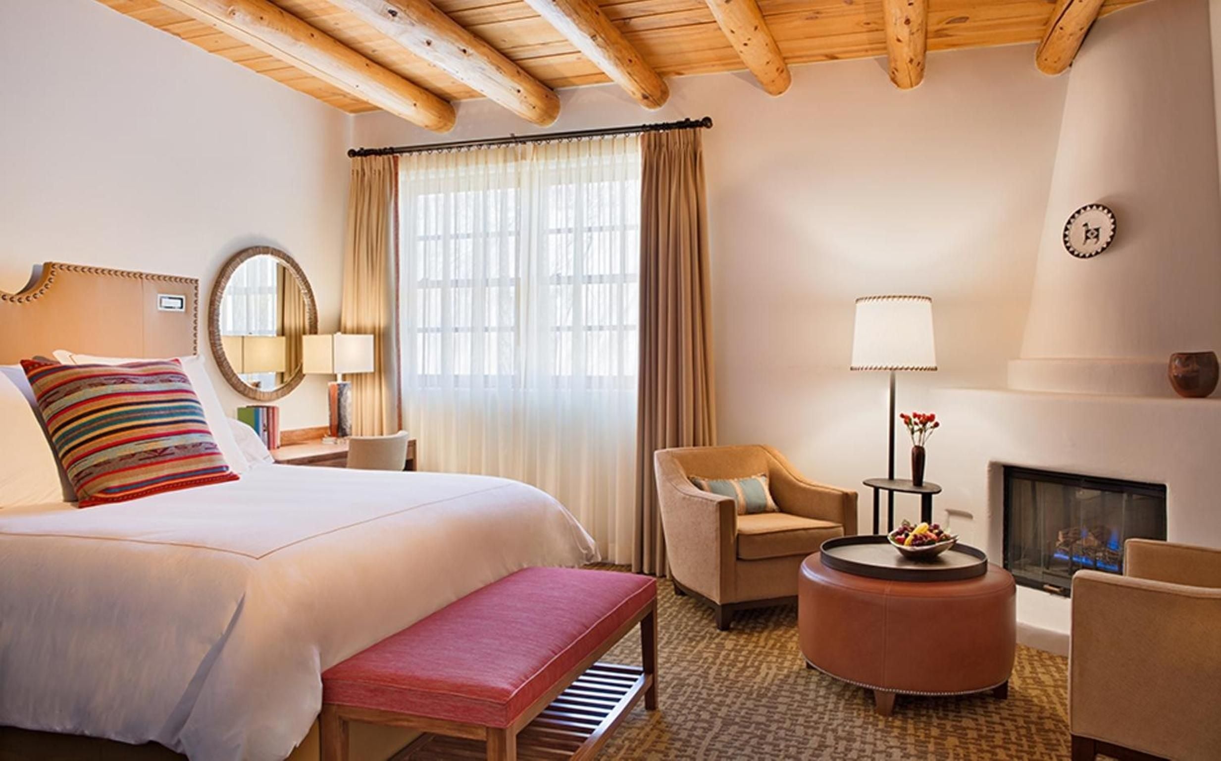 Exposed vigas frame intimate guest quarters where striped textiles and warm adobe walls create a sophisticated Southwest sanctuary, complete with kiva fireplace and handwoven accents.