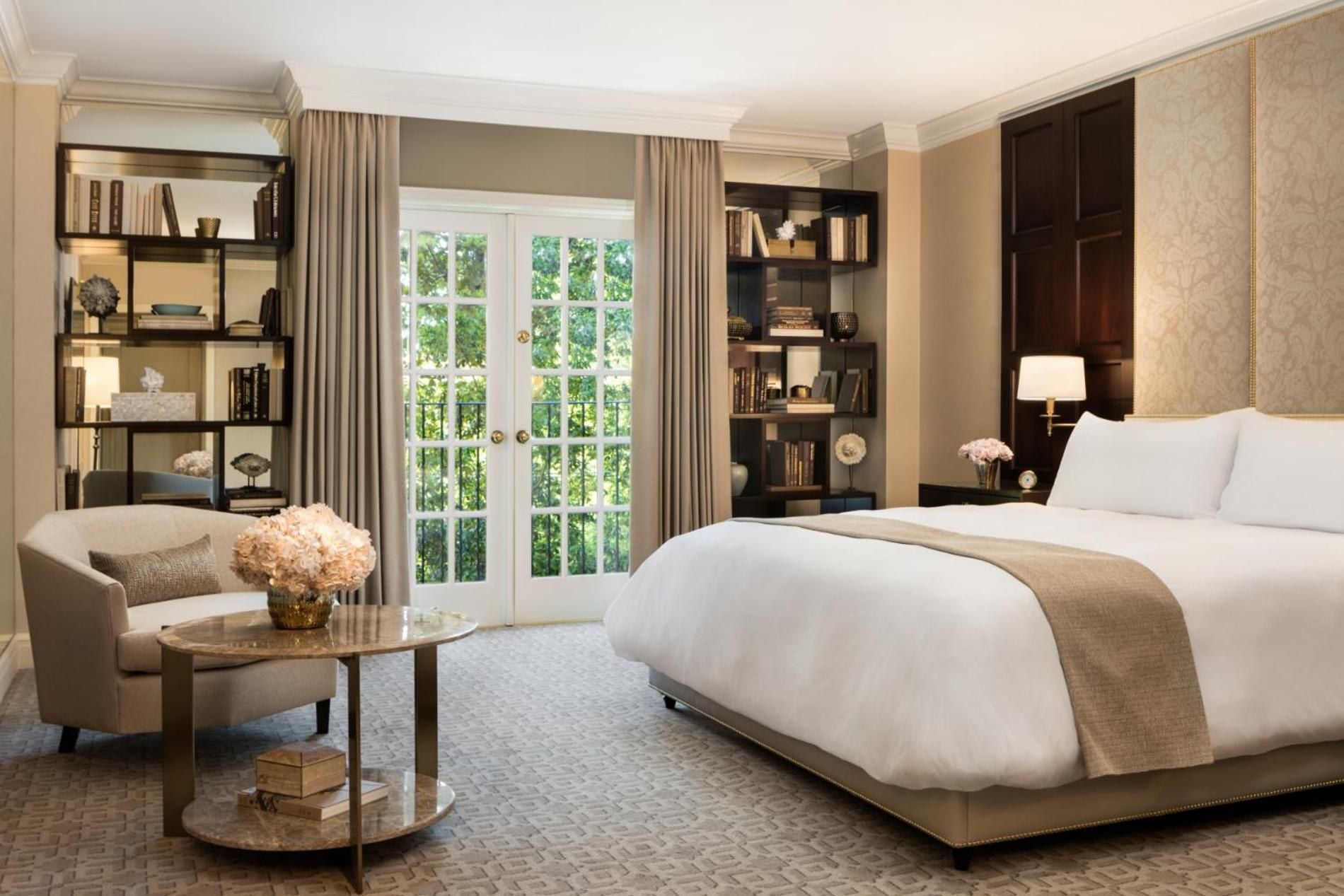 Warm neutrals and rich wood built-ins create an elegant sanctuary, where floor-to-ceiling bookshelves frame French doors opening to verdant garden views.