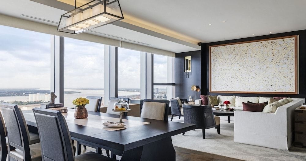 Floor-to-ceiling windows frame Phnom Penh's skyline from this elegant suite, where contemporary furnishings and warm lighting create an intimate sanctuary high above the bustling city.
