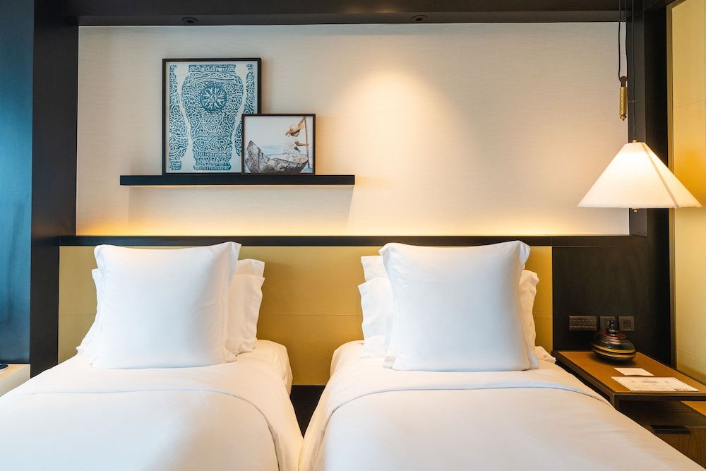 Twin beds showcase crisp white linens against warm amber lighting, while framed artwork and sleek pendant lamps create an intimate, contemporary sanctuary.