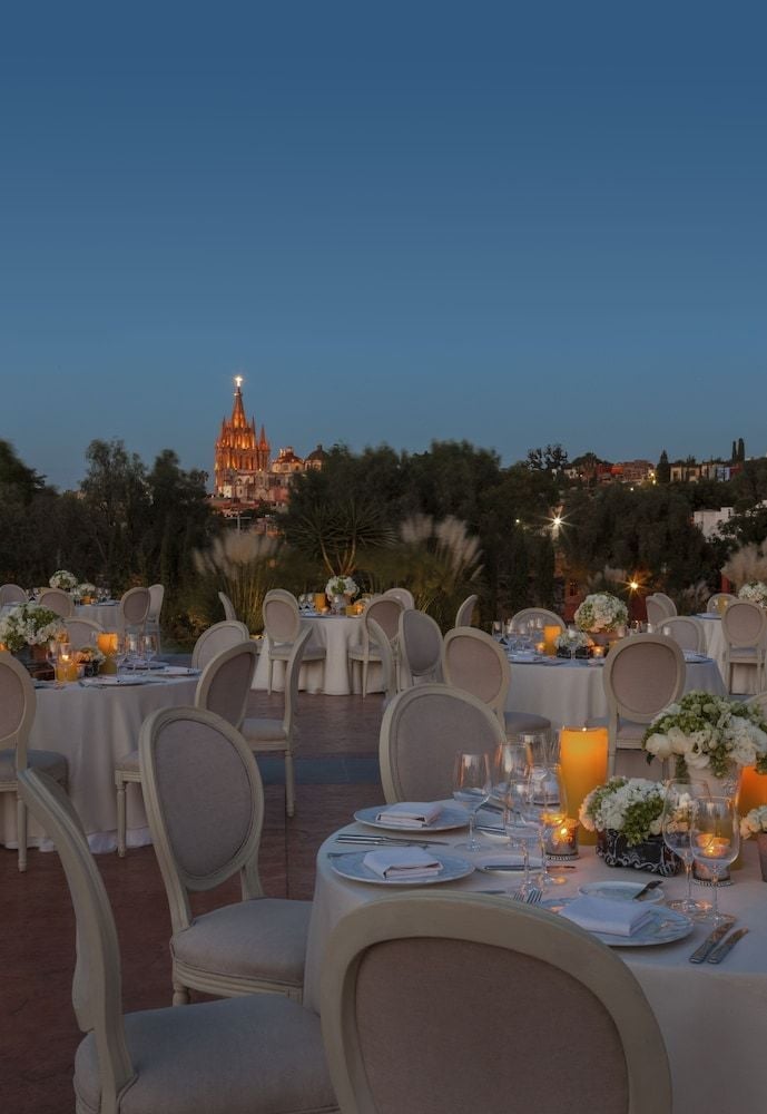 Candlelit tables glow against twilight's embrace as San Miguel's iconic Parroquia cathedral towers majestically beyond this enchanting rooftop dining terrace.