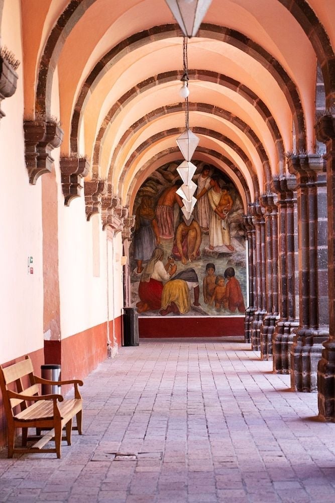 Coral-hued arches frame an ancient corridor where colonial stone meets vibrant murals, creating an intimate gallery that whispers of Mexico's artistic soul.