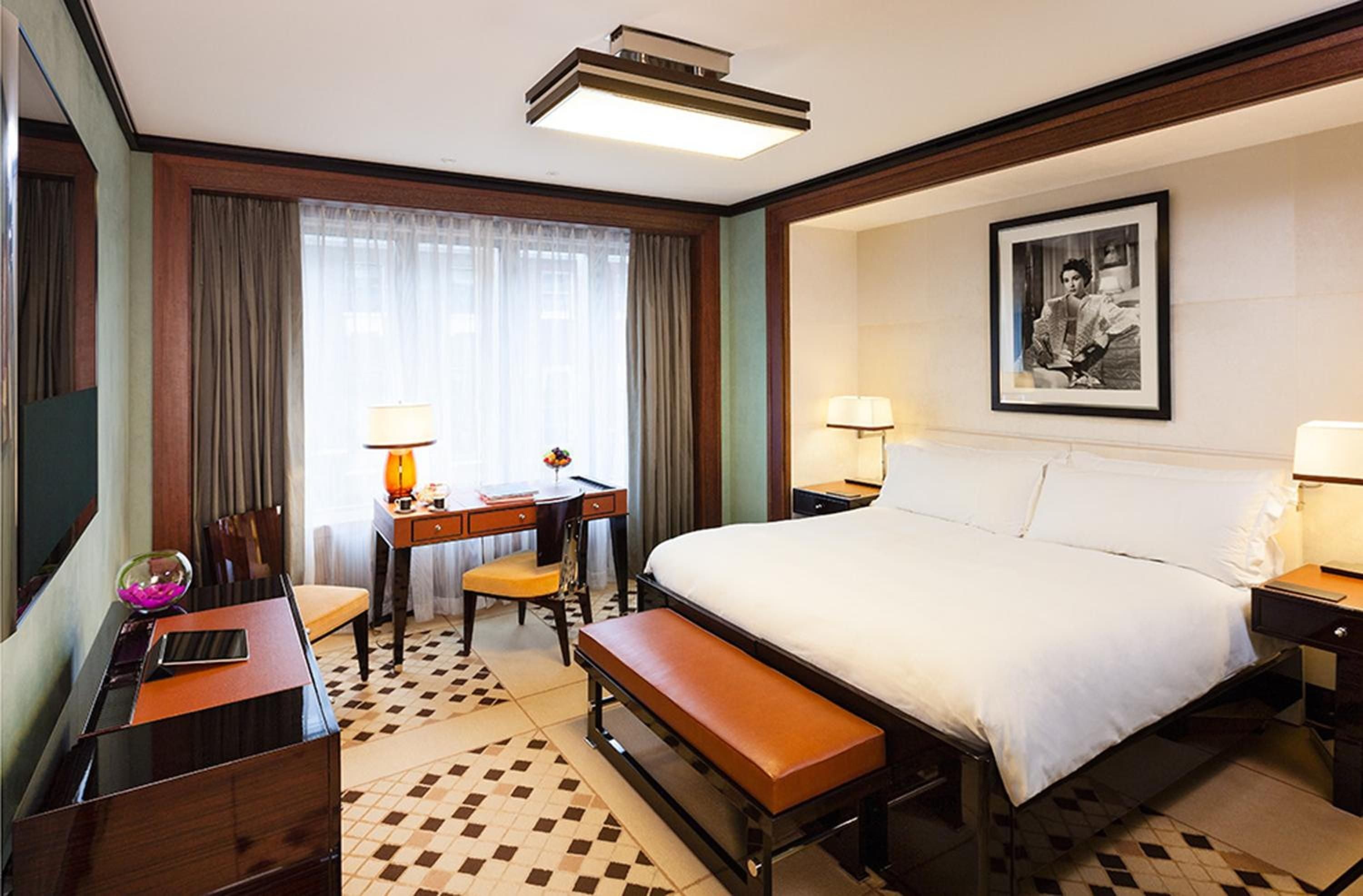 Sophisticated mid-century styling meets modern luxury in this beautifully appointed guest room, where rich wood paneling frames diamond-patterned floors and vintage photography.