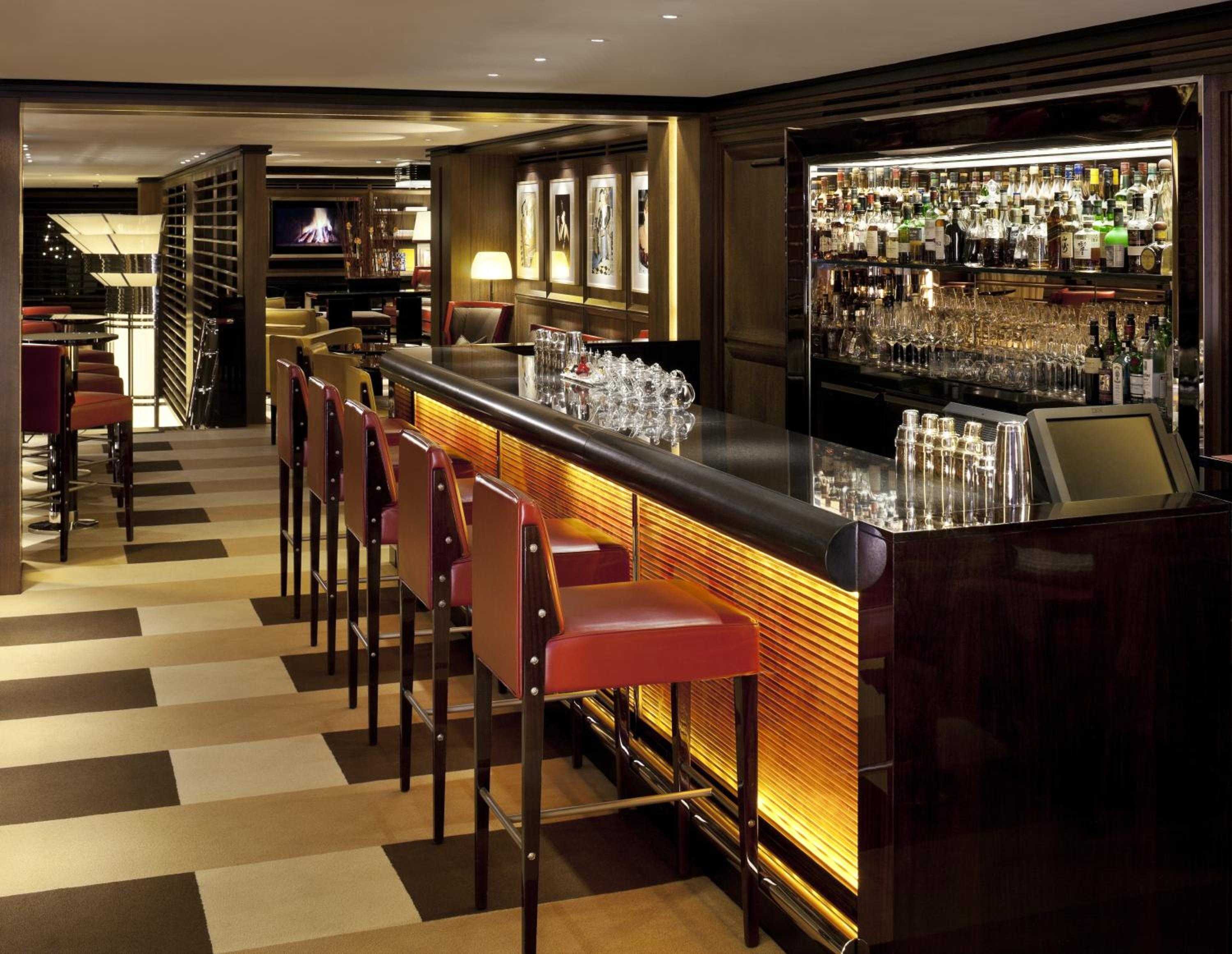 Amber-lit bar stools beckon at this sophisticated drinking den, where backlit bottles create a golden glow against rich wood paneling and polished surfaces.