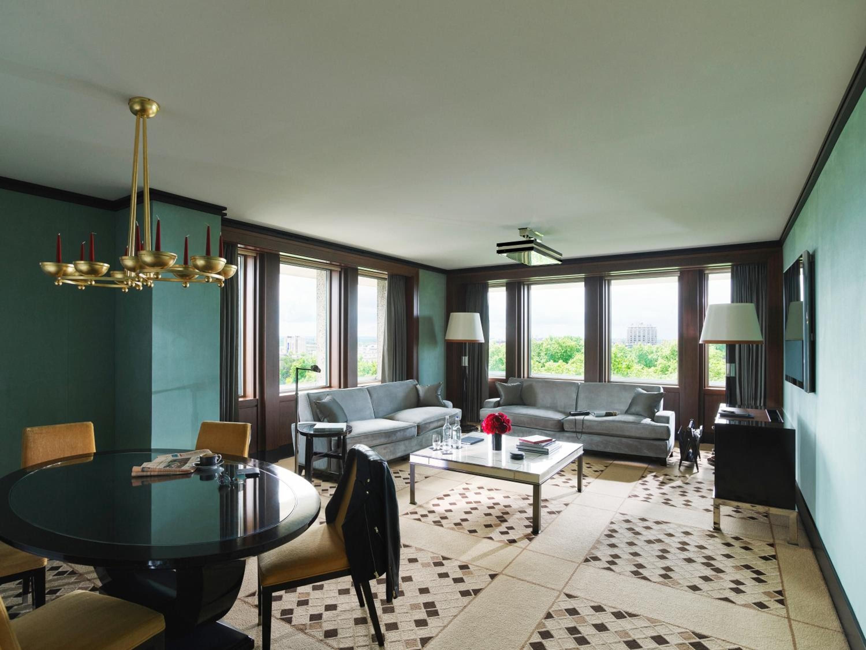 Corner windows frame London's leafy Hyde Park while mint-green walls and dark wood trim create an unexpectedly sophisticated backdrop for plush gray seating and brass accents.
