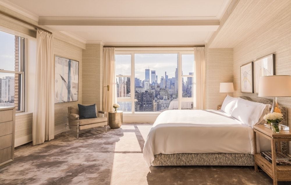 Cream silk curtains frame Manhattan's glittering skyline from this corner suite, where textured grasscloth walls and coffered ceilings create an elegant urban sanctuary.