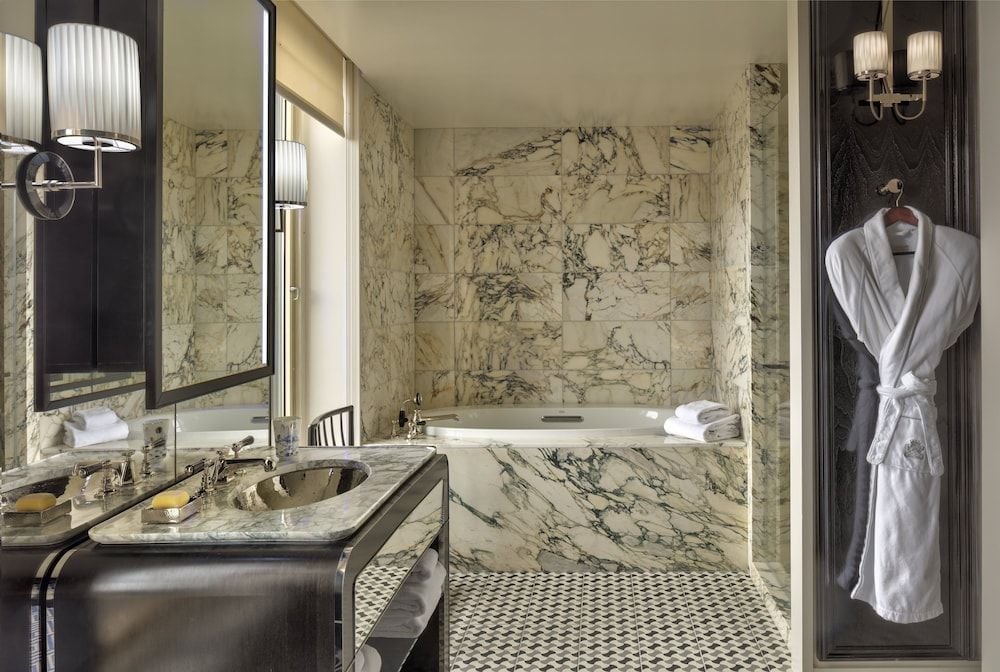 Calacatta marble envelops every surface in this opulent suite bathroom, where geometric floors meet book-matched walls and a pristine white robe awaits.