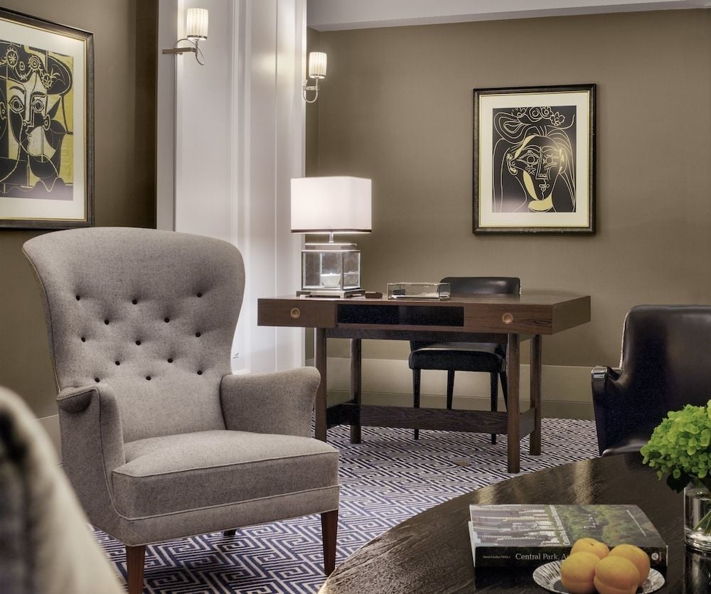 Button-tufted armchairs and Picasso-style prints create an intimate study corner where crystal decanters catch afternoon light streaming through tall windows.