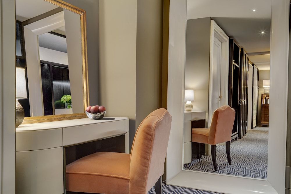Coral velvet chairs and gilt-framed mirrors create intimate dressing alcoves, where geometric carpets and warm lighting evoke Upper East Side sophistication.