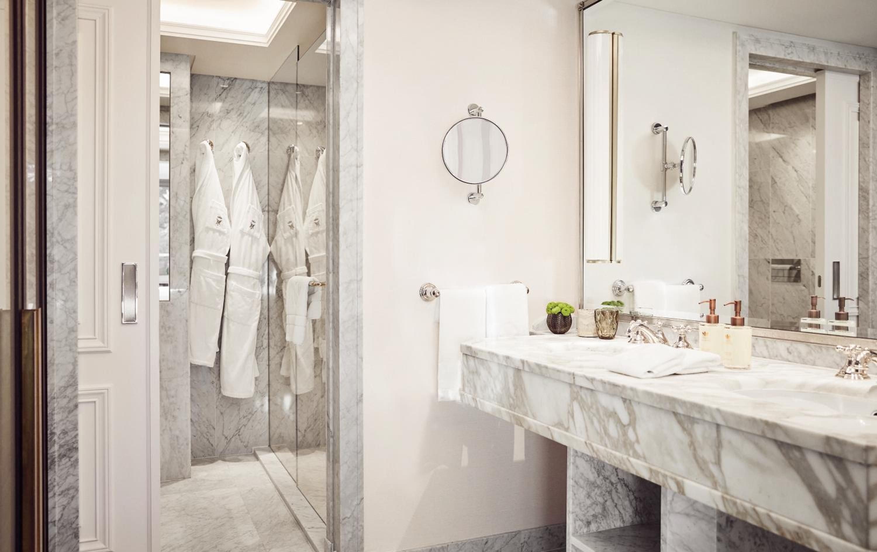 Carrara marble gleams throughout the palatial bathroom where plush robes await and natural light streams through skylights, creating an intimate spa sanctuary.