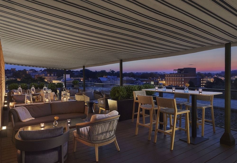 Lanterns flicker across CUT DC's rooftop terrace as twilight paints Georgetown's skyline, where woven chairs and plush seating create intimate corners above the capital.