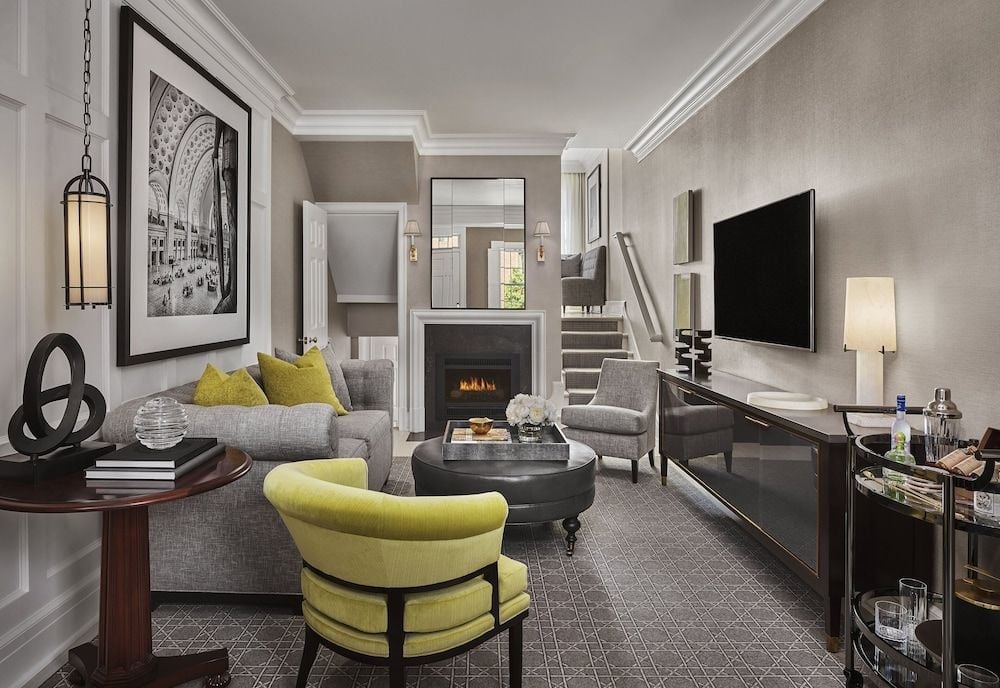 Charcoal-gray walls and chartreuse accents create sophisticated drama in this duplex suite, where crown molding frames a crackling fireplace and floating staircase leads to intimate quarters above.